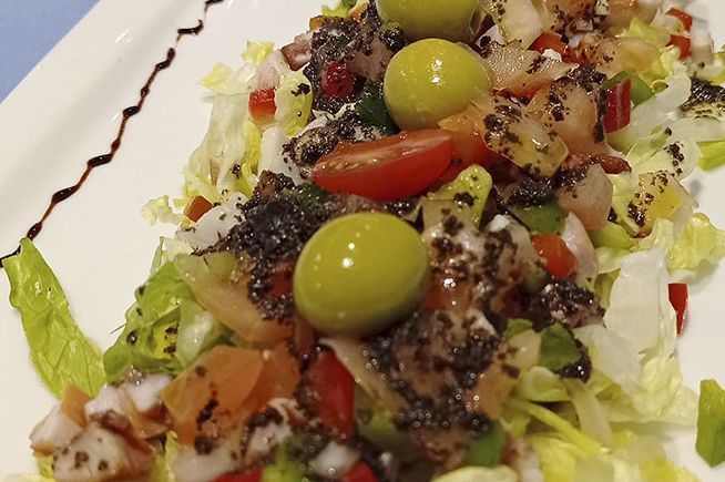 Un primer plano de una ensalada con aceitunas, tomates y lechuga en un plato blanco.