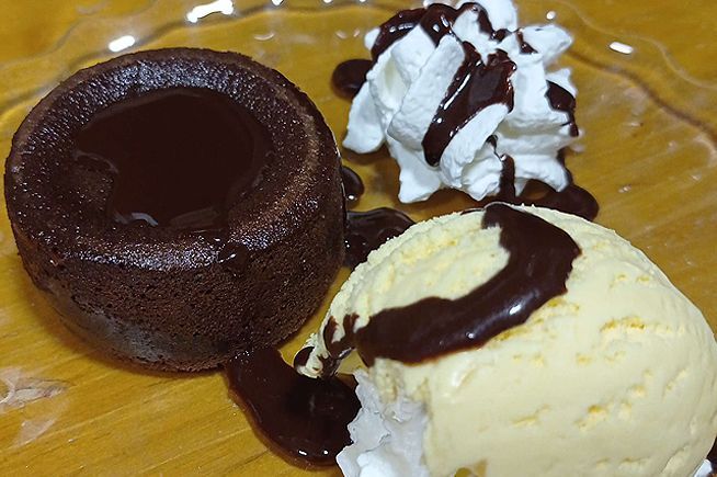 Un pastel de chocolate con crema batida y salsa de chocolate junto a una bola de helado.
