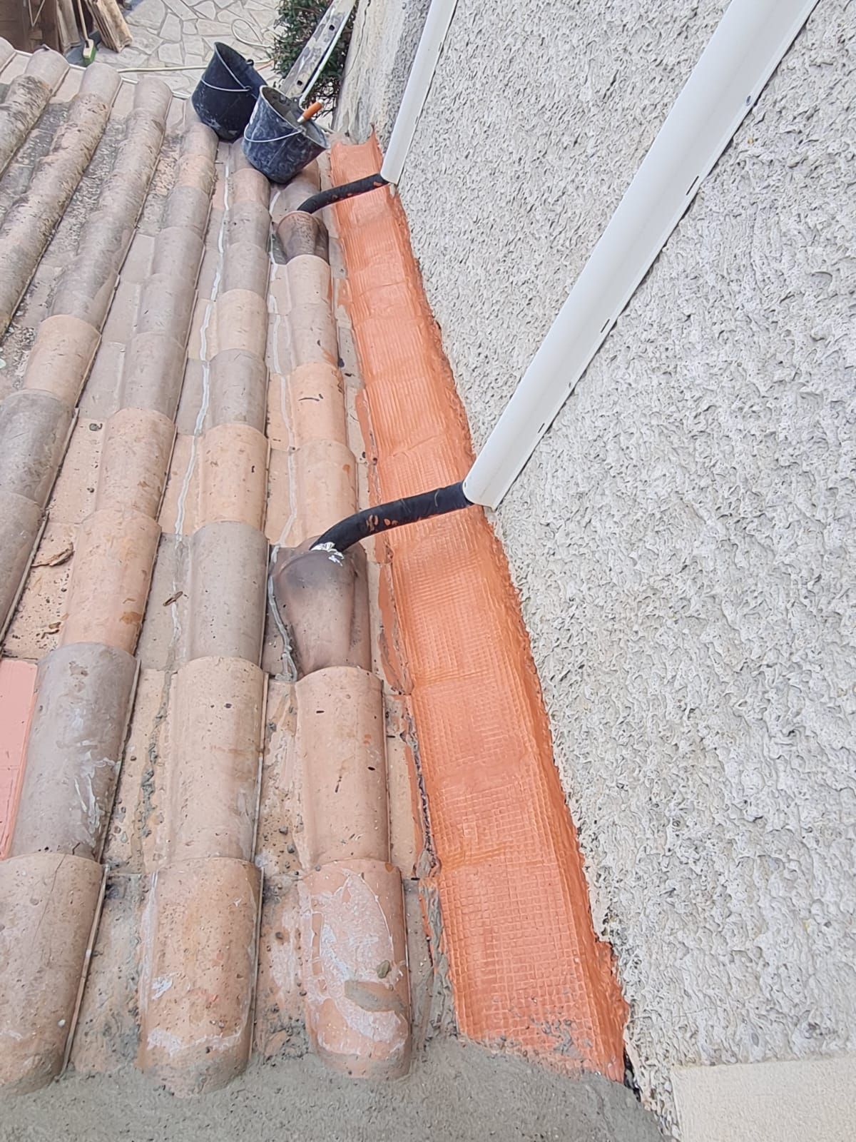 Une section de toiture montrant un tuyau de descente blanc menant à une zone de solin étanche orange.