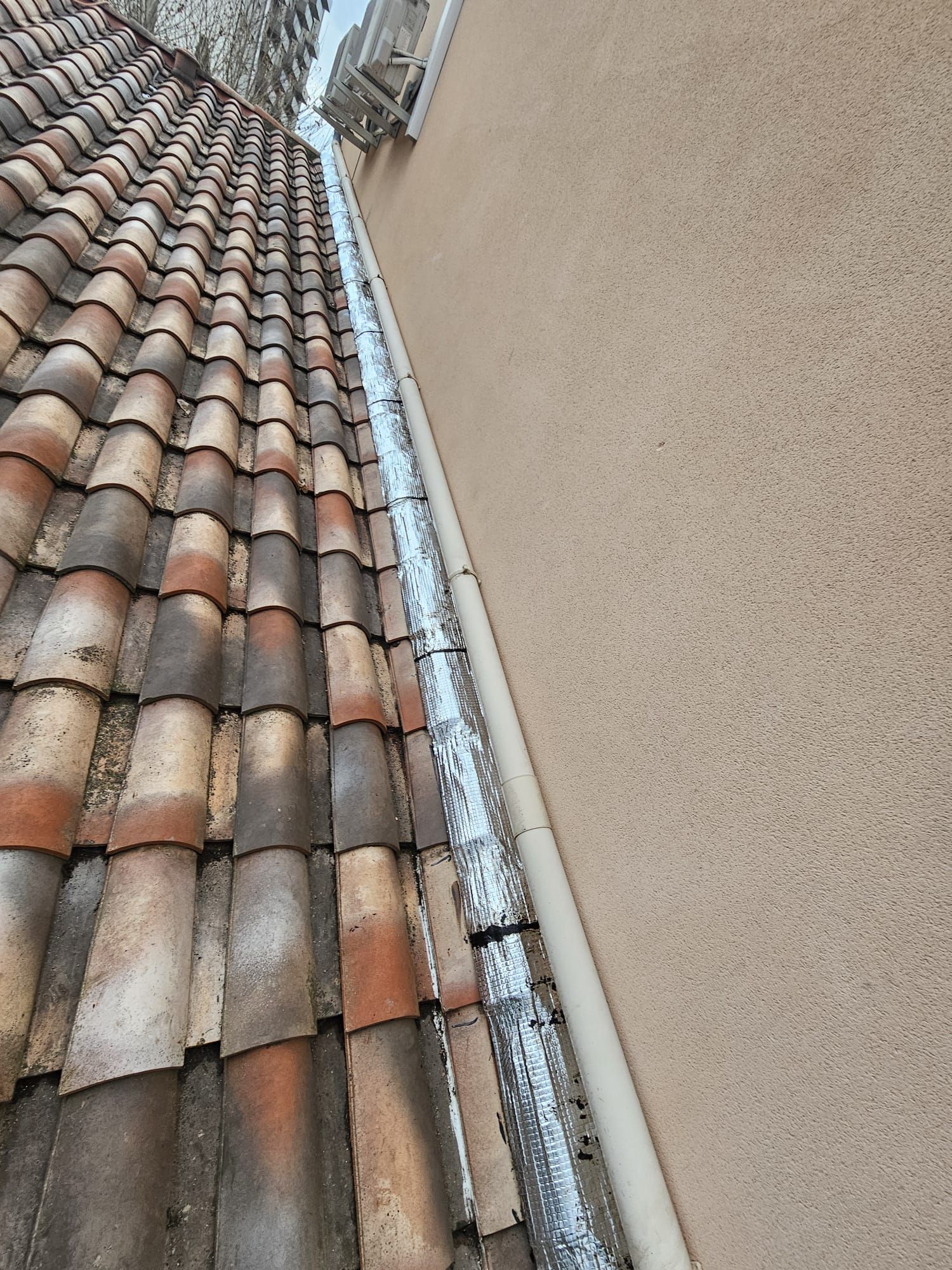 Un toit de tuiles rejoint un mur en stuc, avec un canal d'évacuation métallique.