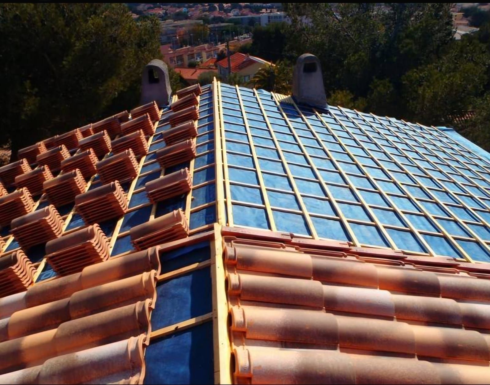 Toiture d'une maison en rénovation, avec des liteaux en bois apparents, une membrane d'étanchéité bleue et des tuiles.