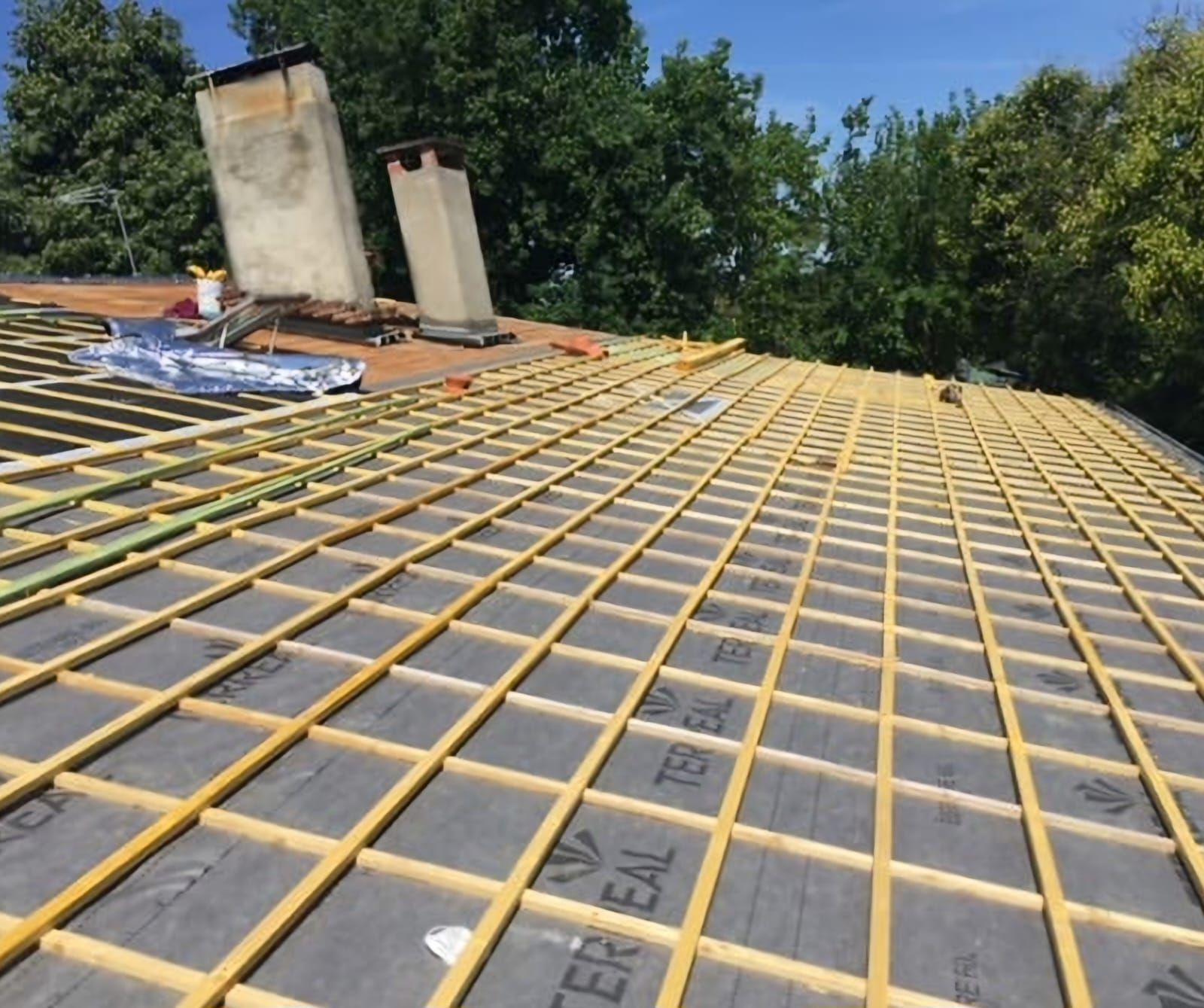 Une toiture en construction, constituée d'une grille de liteaux en bois installée sur une membrane d'étanchéité noire.