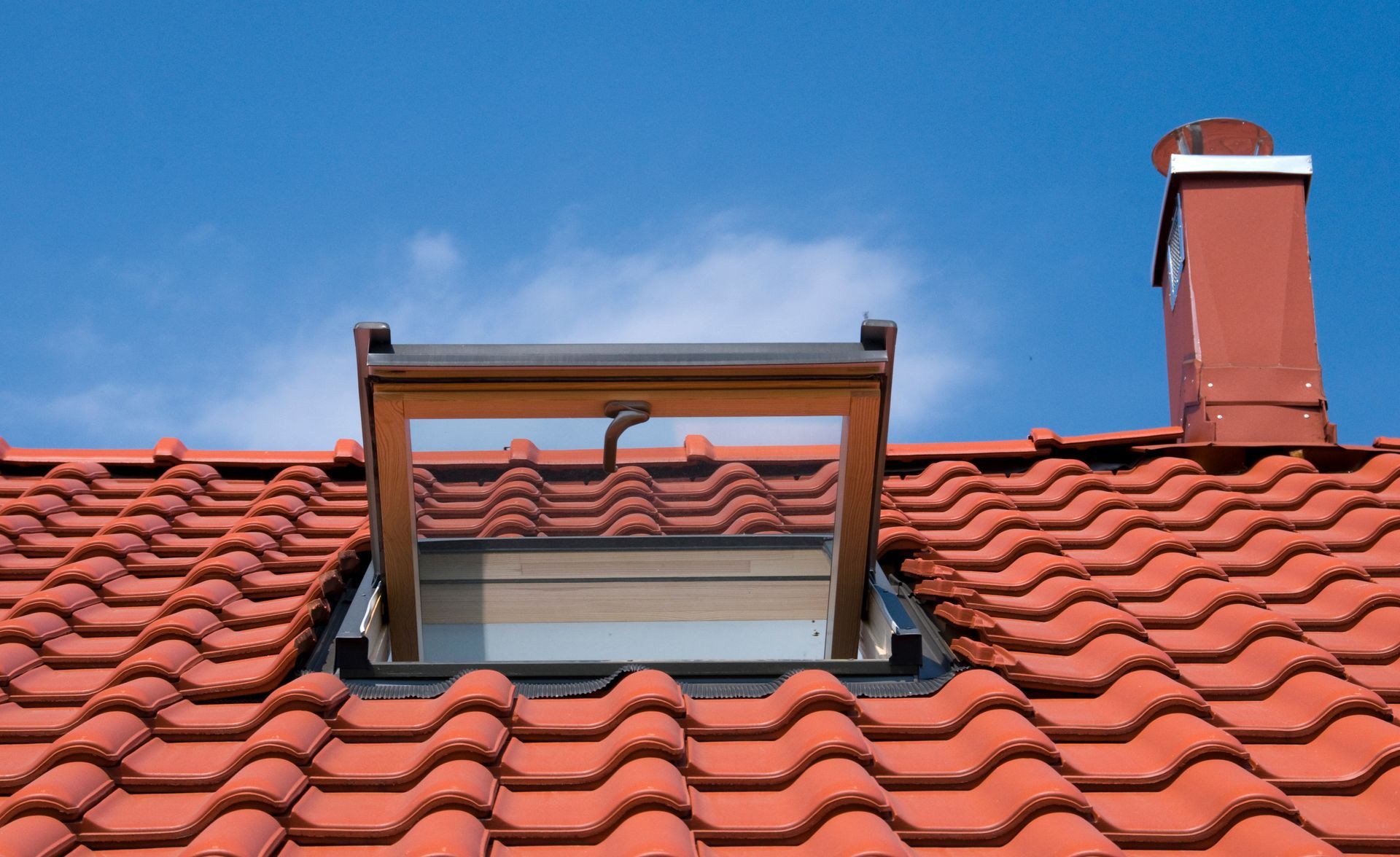Fenêtre de toit ouverte sur un toit de tuiles rouges.