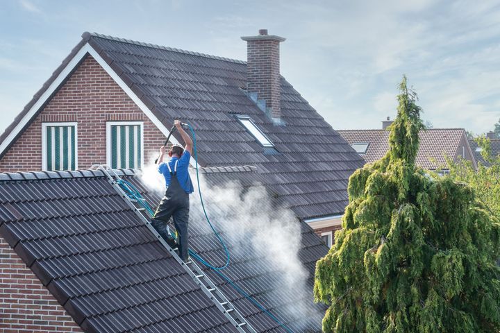 Une personne nettoie un toit sombre au nettoyeur à haute pression.