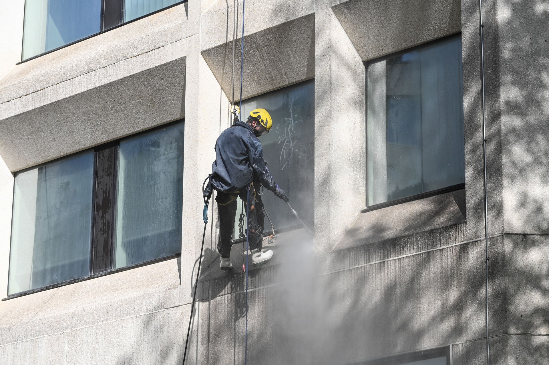 Un artisan, suspendu par des cordes, nettoie la façade d'un bâtiment.