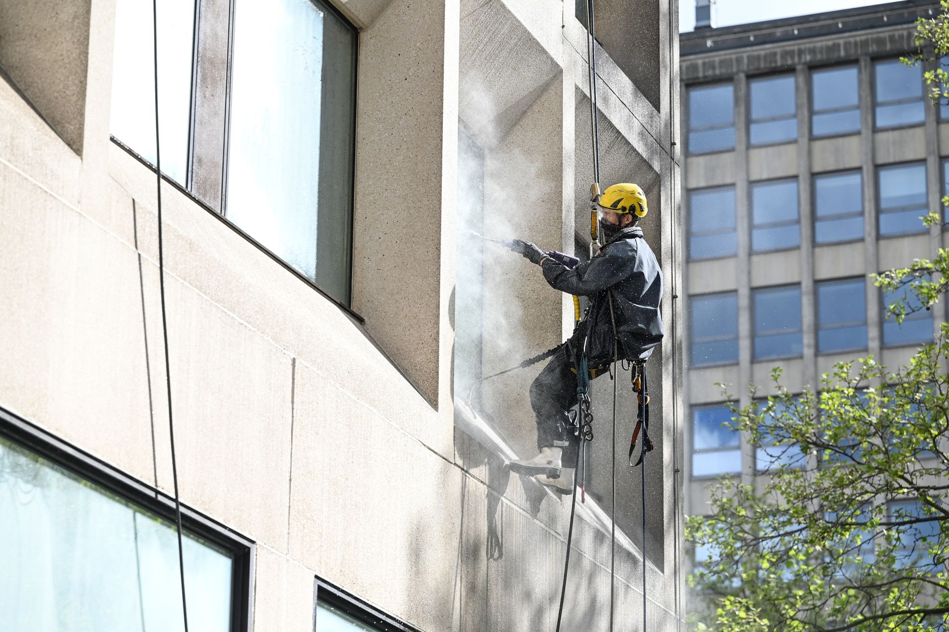 Un ouvrier portant un harnais de sécurité nettoie l'extérieur d'un bâtiment.