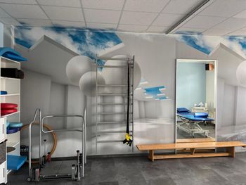 Fitnessraum mit Trainingsgeräten, Wandspiegeln und einer lichtdurchfluteten Decke mit Wolkenmotiv.