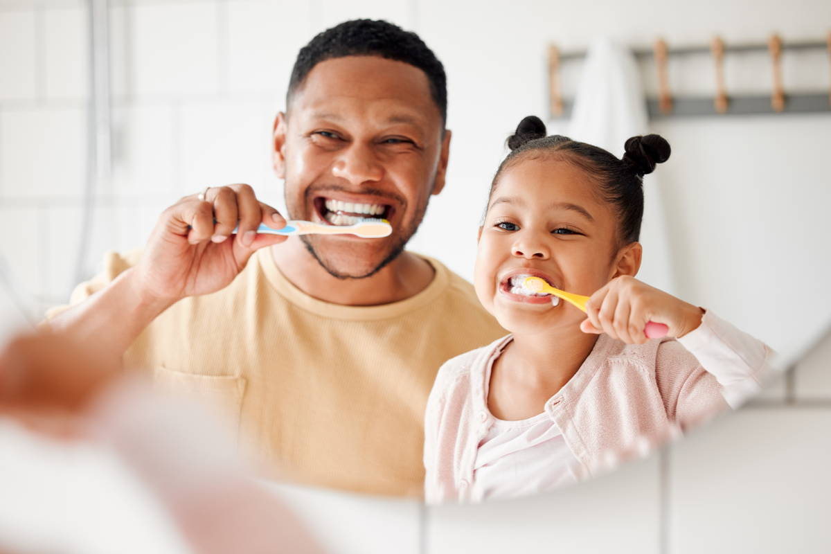 Homme et petite fille se brossant les dents devant un miroir