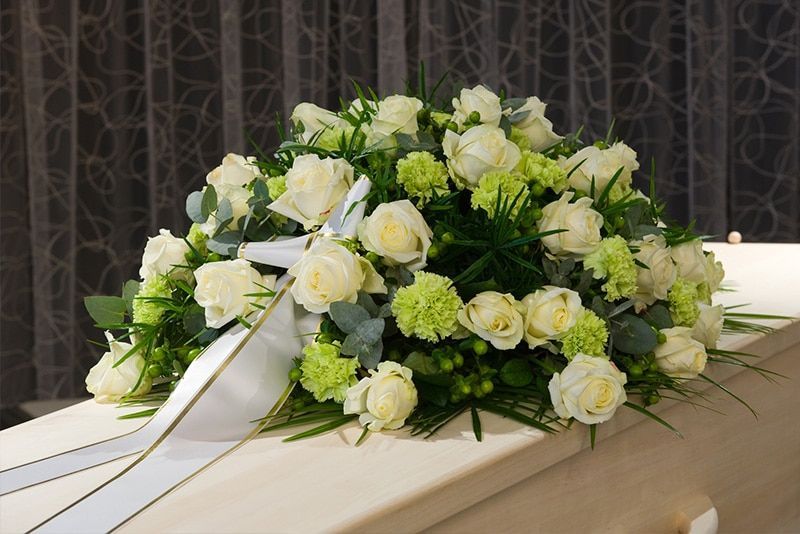 Un ataúd con rosas blancas y claveles verdes encima.