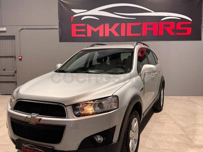 Un SUV Chevrolet plateado en una sala de exposición, estacionado frente a un letrero de EMKICARS.