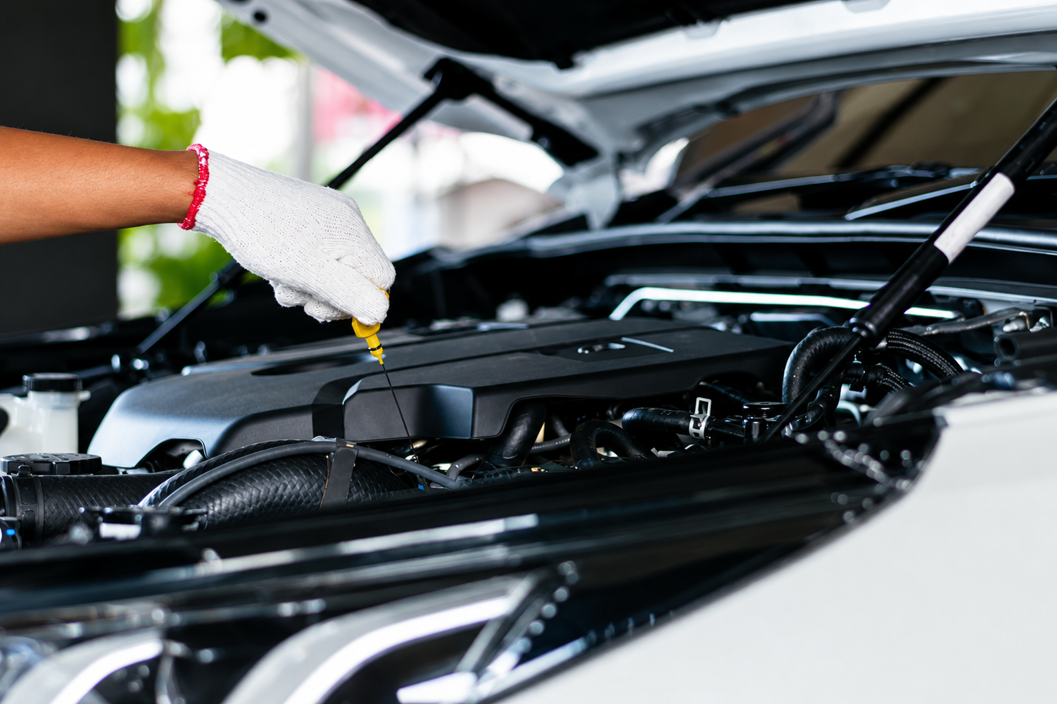Una mano enguantada inspecciona el motor del coche bajo el capó abierto.