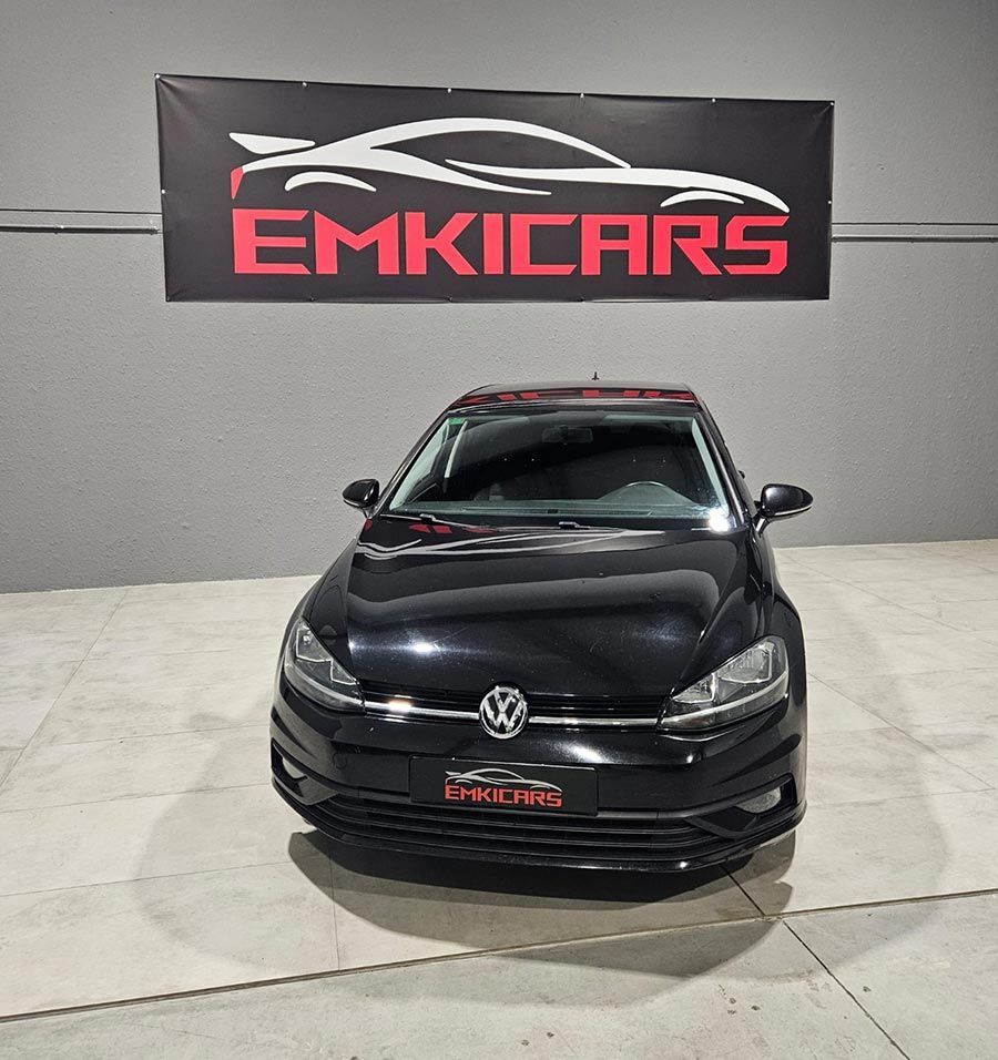 Un Volkswagen hatchback negro estacionado en el interior, bajo una pancarta de EMKICARS.