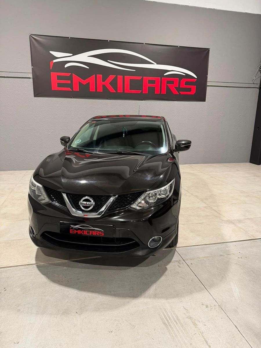 Un SUV Nissan negro se exhibe en el interior, frente a un cartel del concesionario EmKcars.