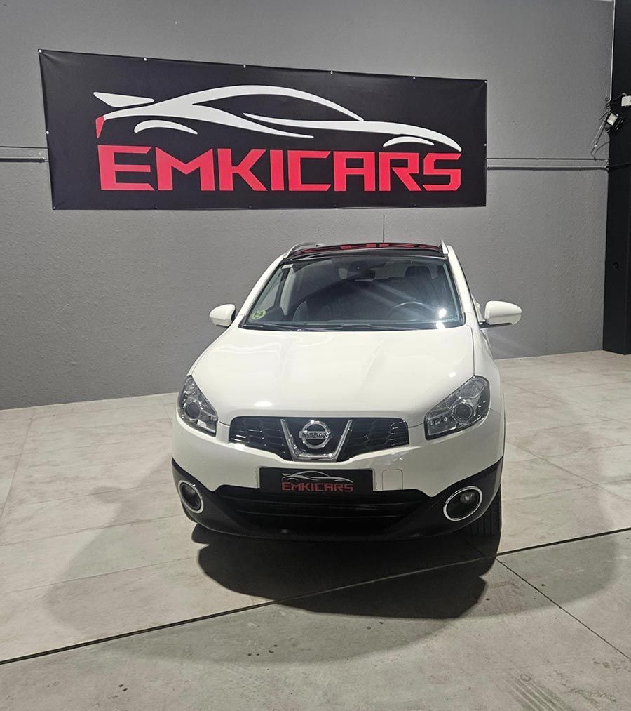 SUV Nissan blanco estacionado frente a un letrero de un concesionario EMKICARS