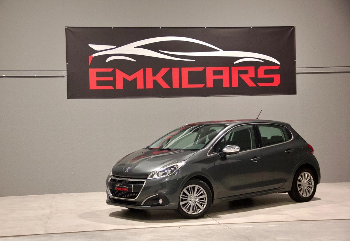 Coche hatchback gris oscuro aparcado en el interior, debajo de un letrero de EMKICARS.
