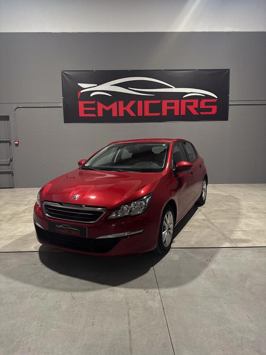 Coche hatchback rojo aparcado en el interior, delante de una pancarta de EMKICARS.