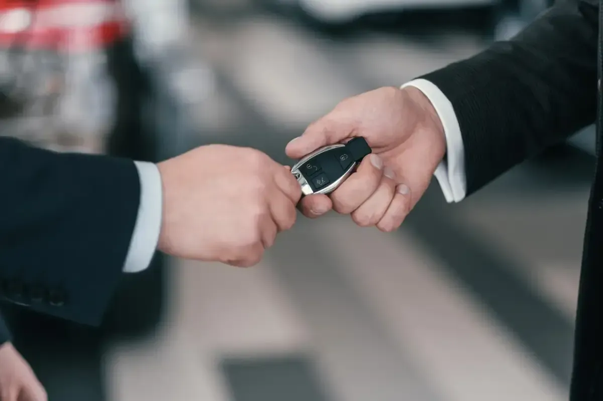 Dos empresarios intercambian las llaves de un coche en un interior borroso.
