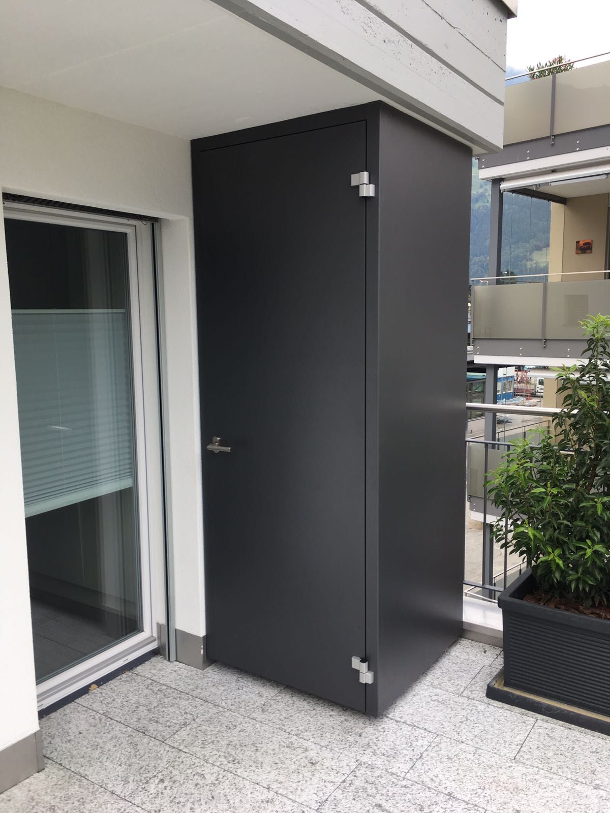 Schwarze Tür zu einem Balkon oder Abstellraum auf einer grau gefliesten Wohnungsterrasse