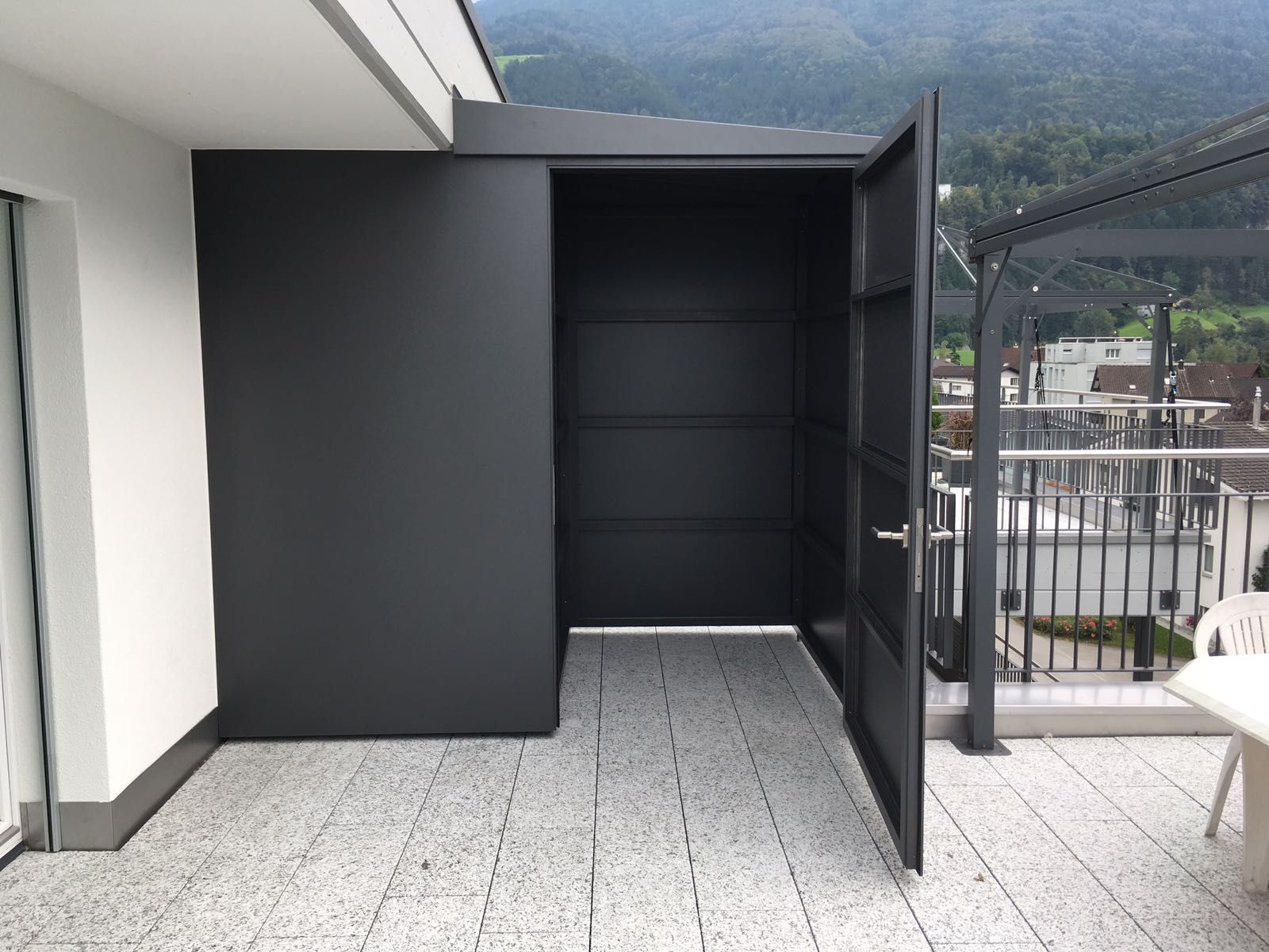 Offener schwarzer Aufbewahrungsschrank auf einem Balkon mit Bergblick.
