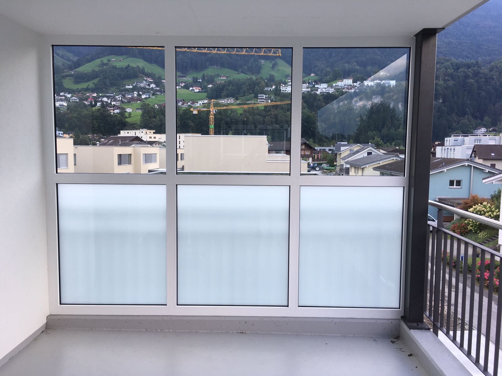 Geschlossener Balkon mit Milchglasscheiben und Blick auf die dahinterliegenden Berge.