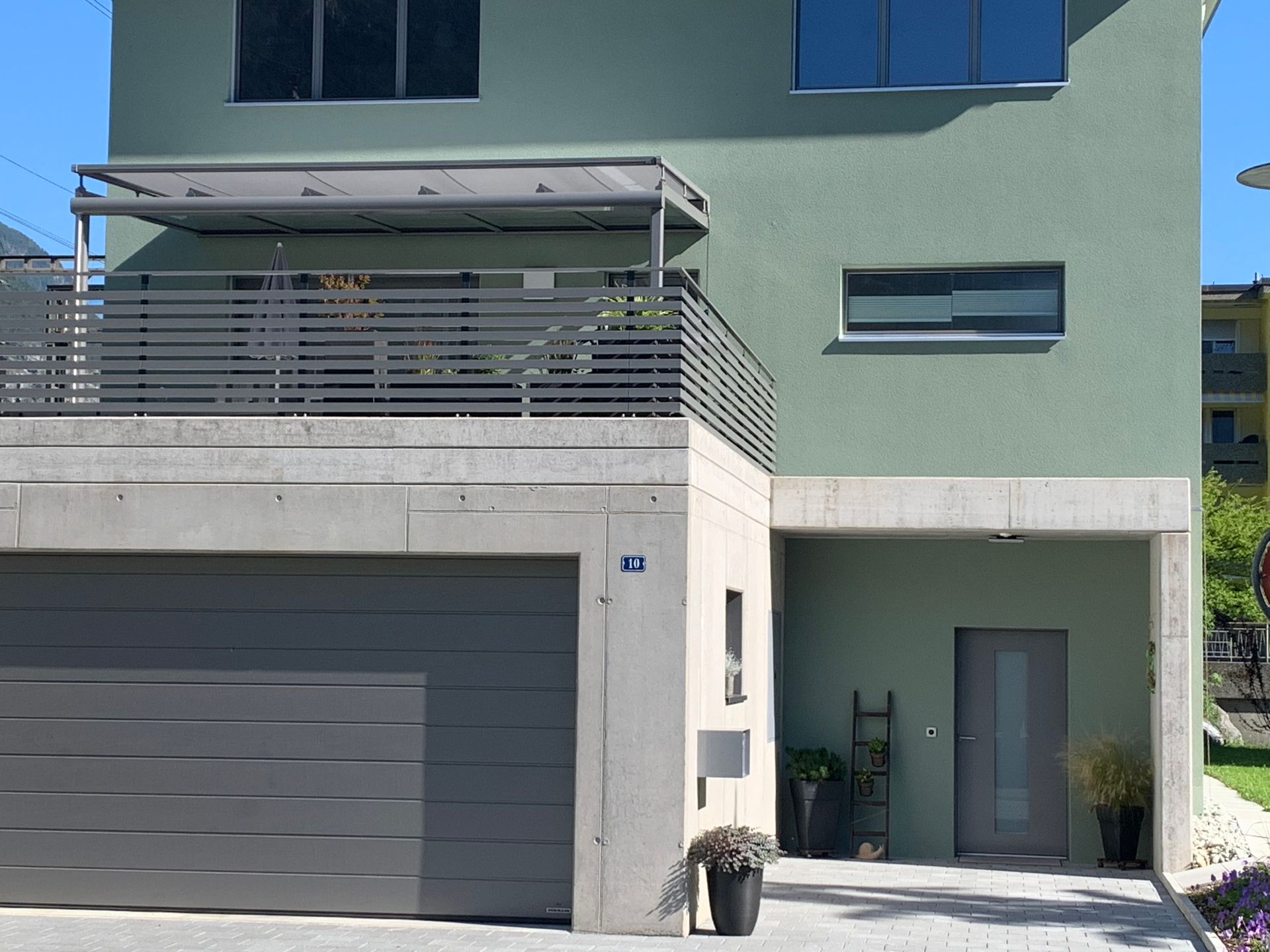 Moderne Wohnungsfassade mit grauem Garagentor, Balkon und Seiteneingang an einem sonnigen Tag