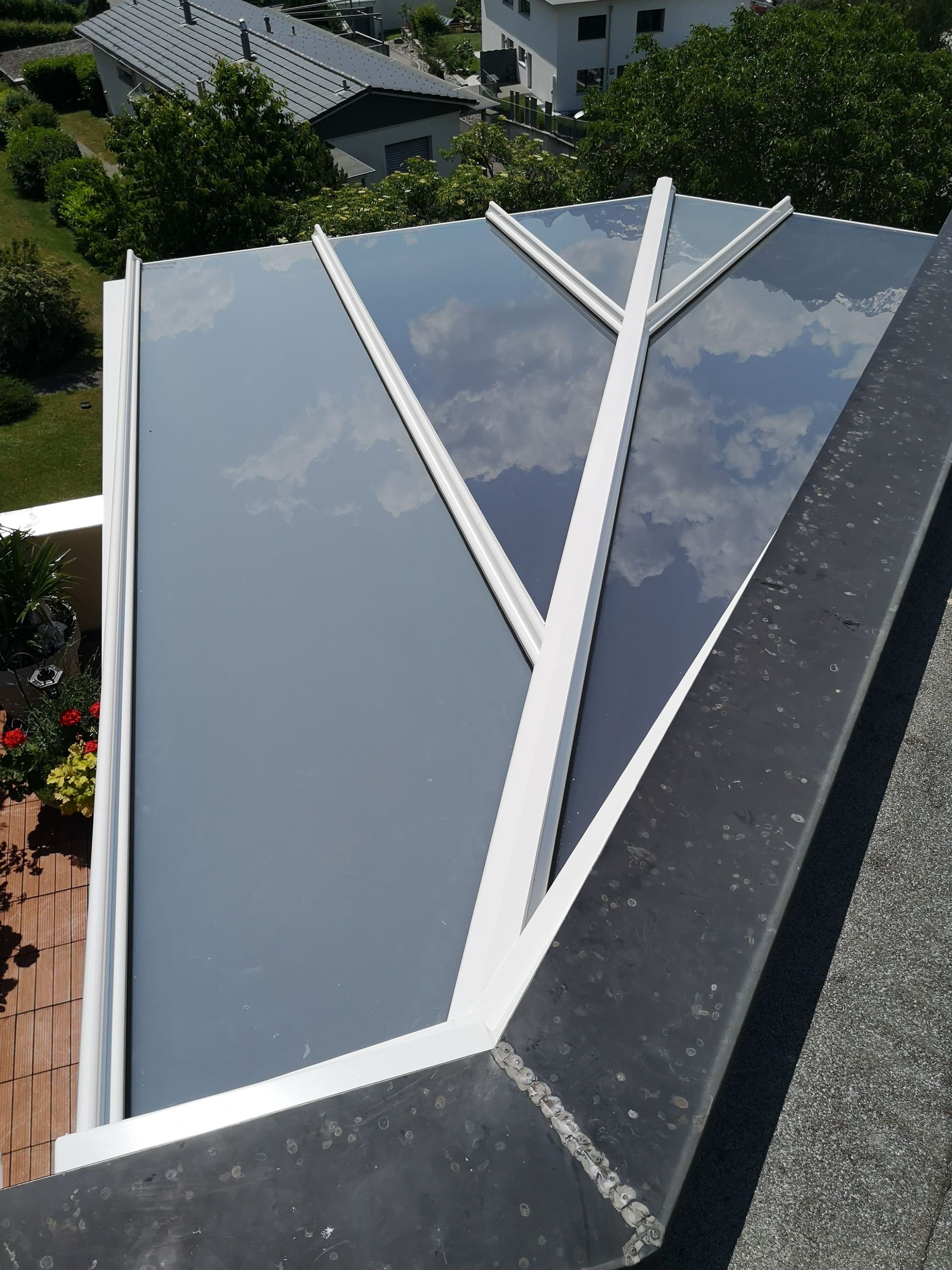 Modernes Dachfenster mit weissem Rahmen und reflektierenden Glasscheiben unter bewölktem Himmel