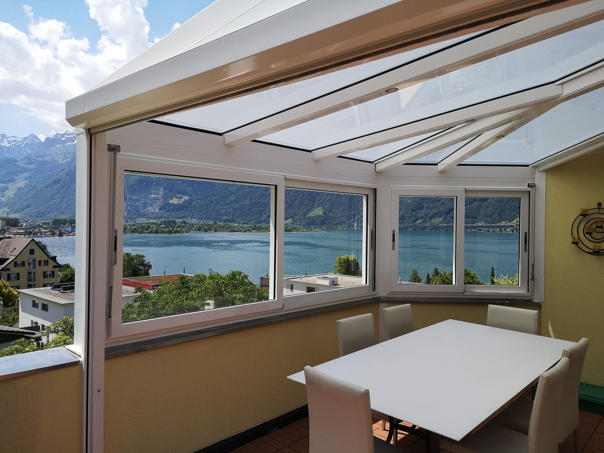 Sonnendurchfluteter, geschlossener Terrassen-Essbereich mit Blick auf einen See und die Berge