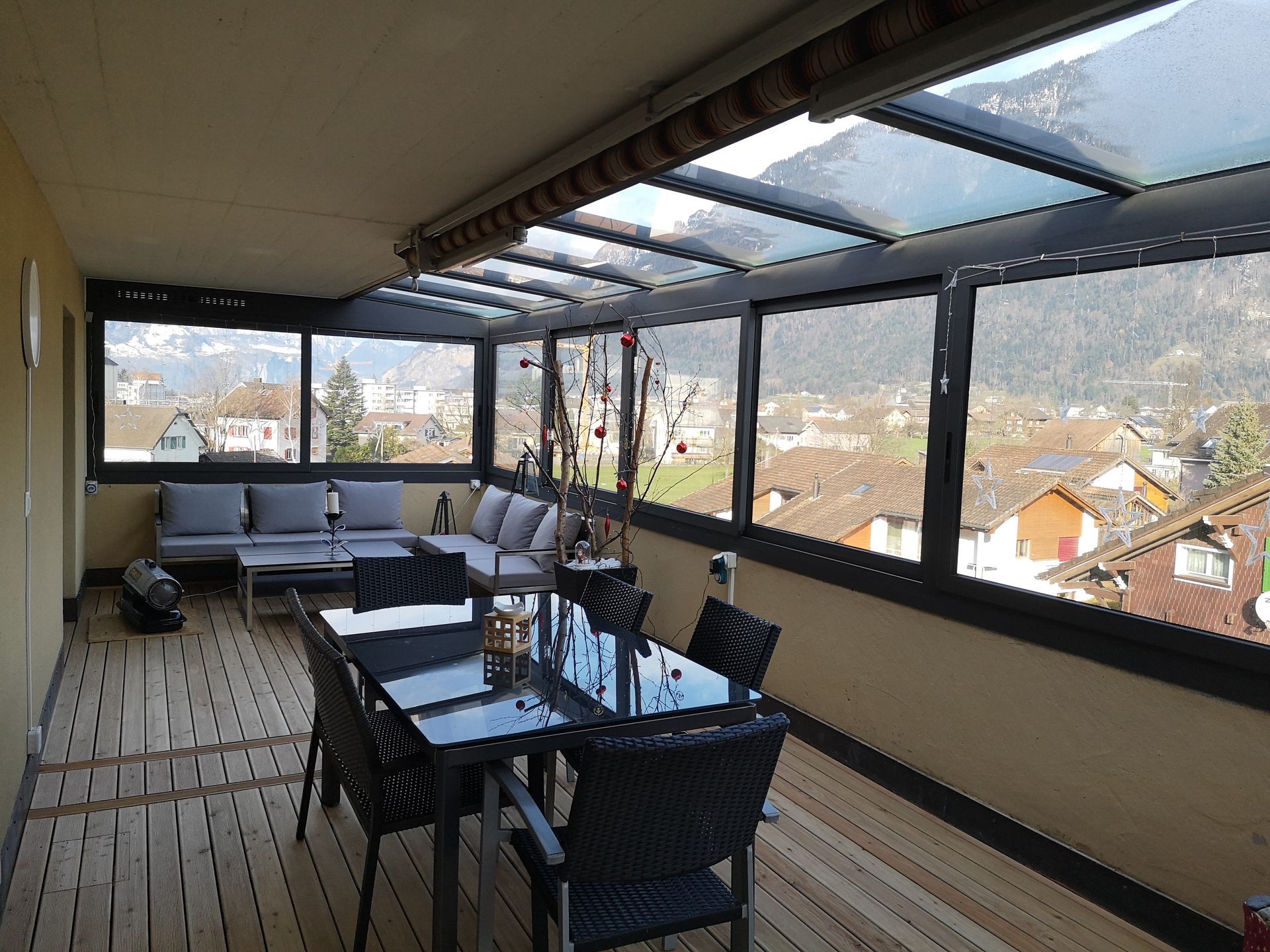 Überdachte Dachterrasse mit Glasgeländer, Esstisch, Stühlen und Bergblick bei Sonnenuntergang