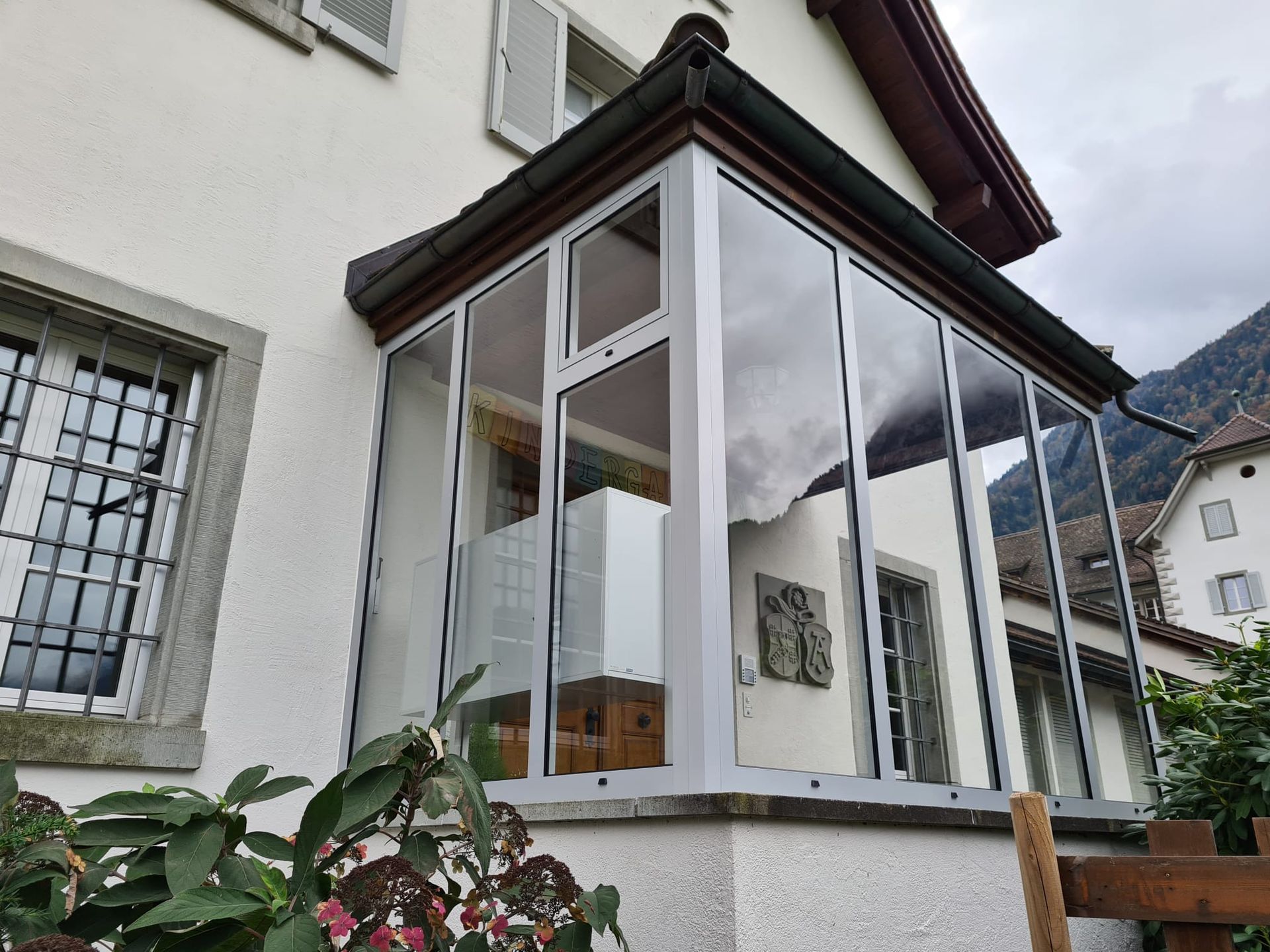 Verglaste Veranda an einem weissen Haus mit Bergen im Hintergrund