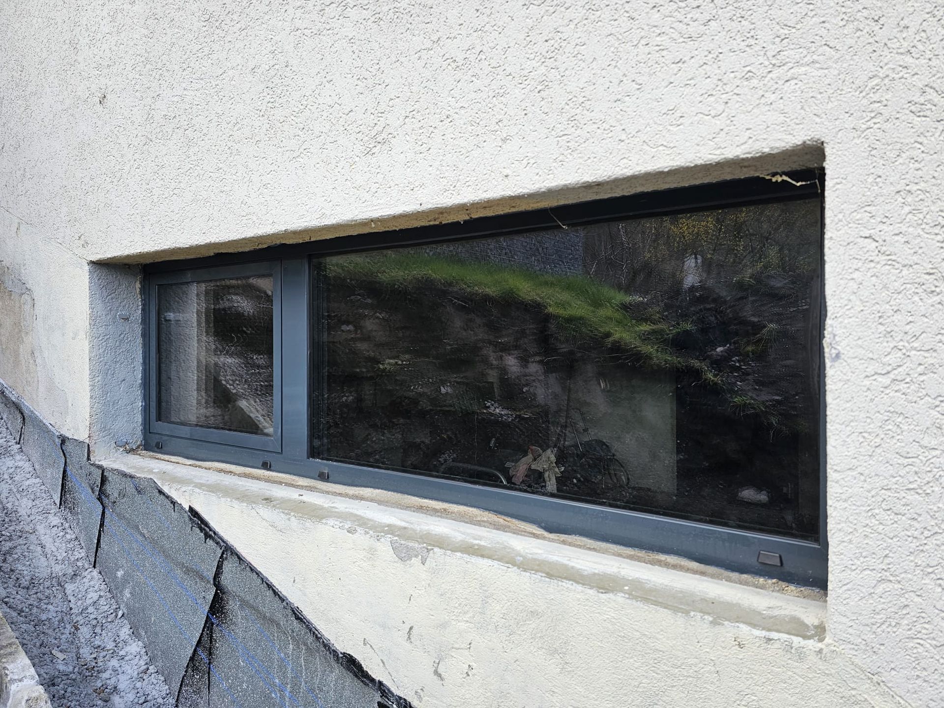 Schmale Kellerfenster in einer weissen Stuckwand über einem grauen Steinfundament.