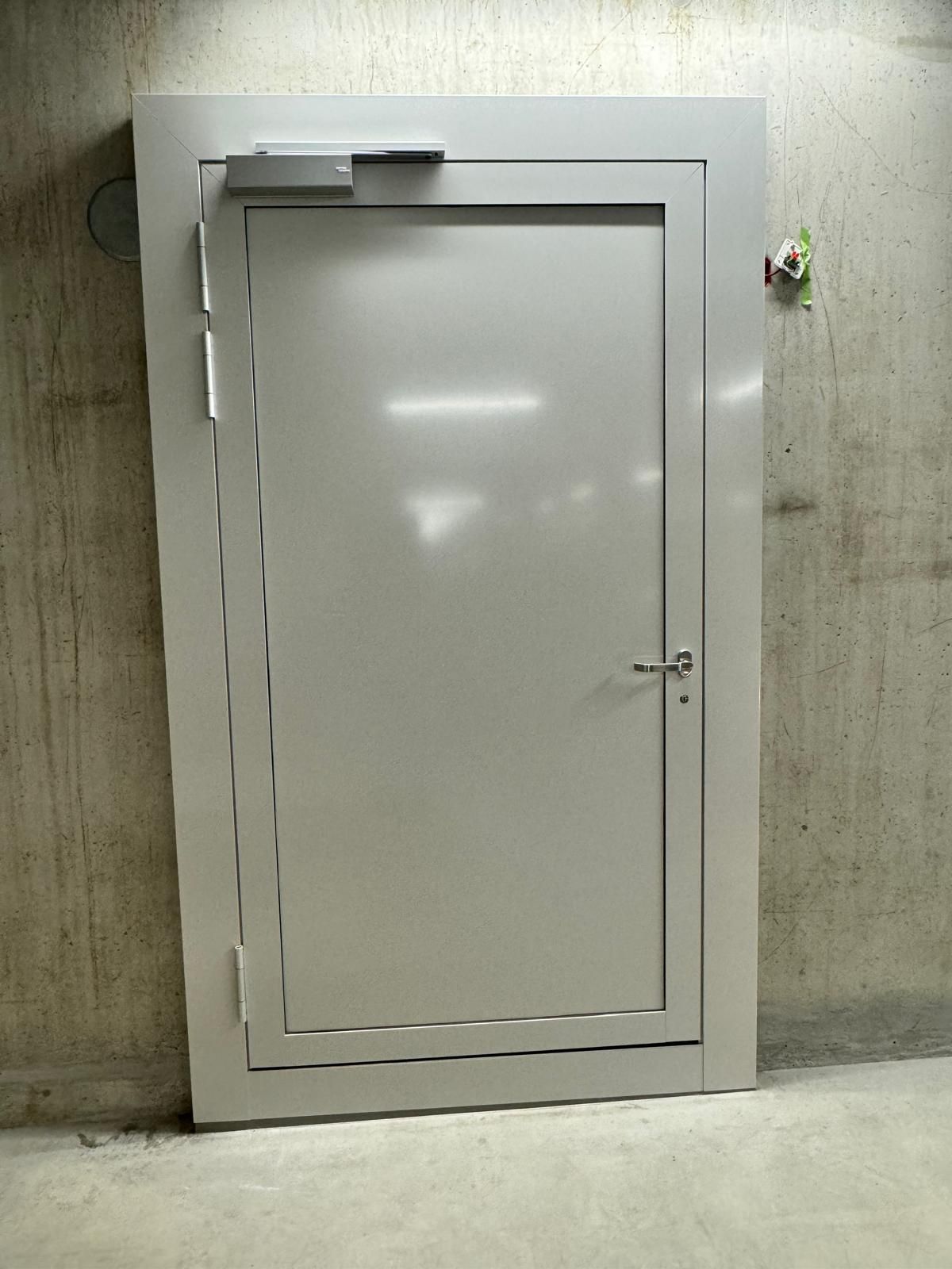 Weisse Metalltür in einer Betonwand mit kleinem Türschliesser oben.