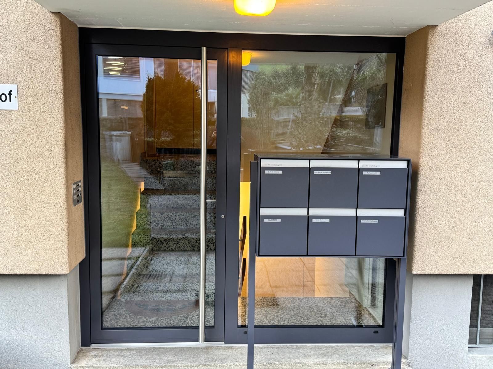 Eingang zum Wohnhaus mit Glastüren und einer an der Wand montierten Briefkastenanlage