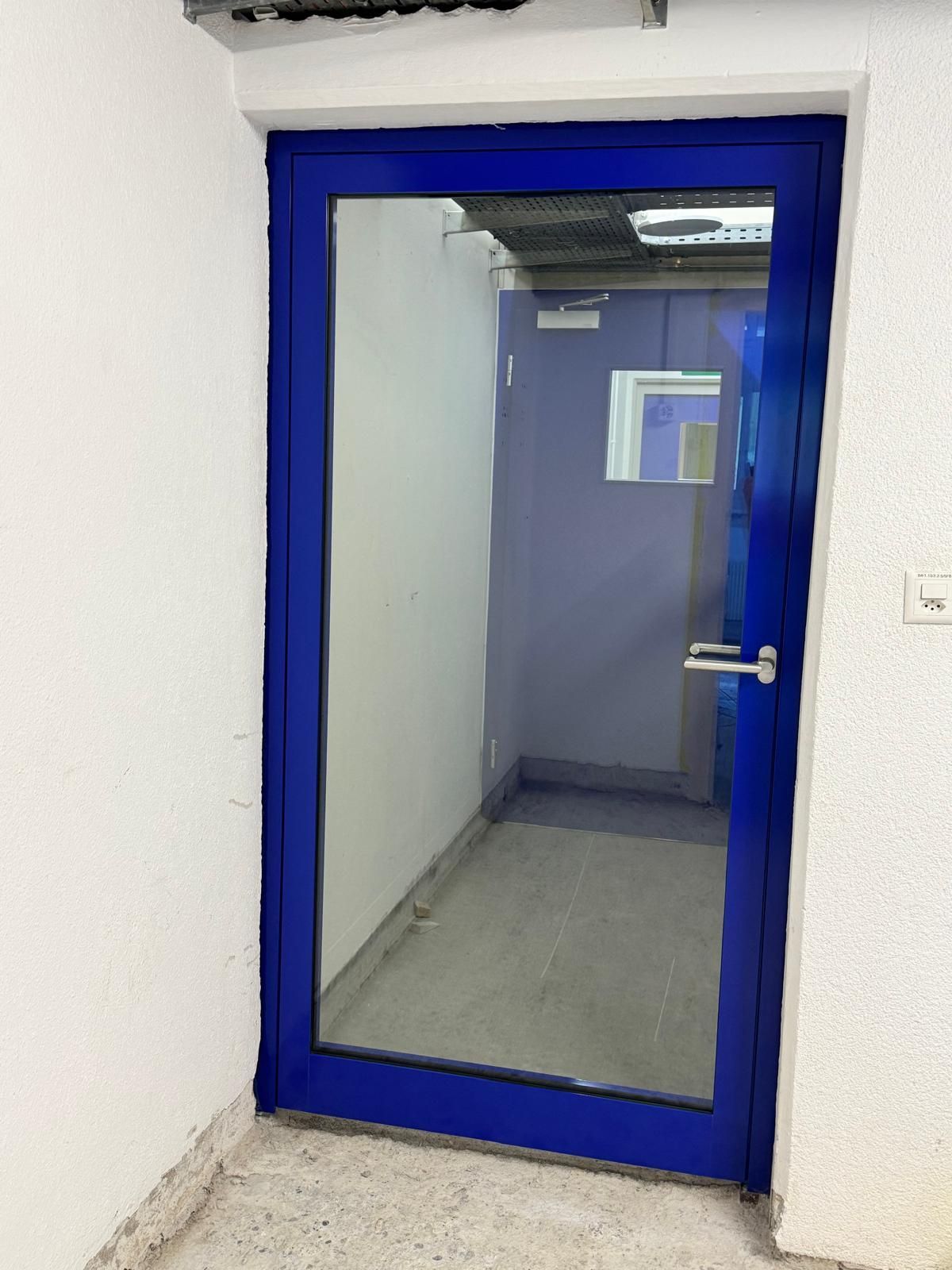Eine blau umrandete Glastür öffnet sich zu einem schmalen Flur oder Zimmer.