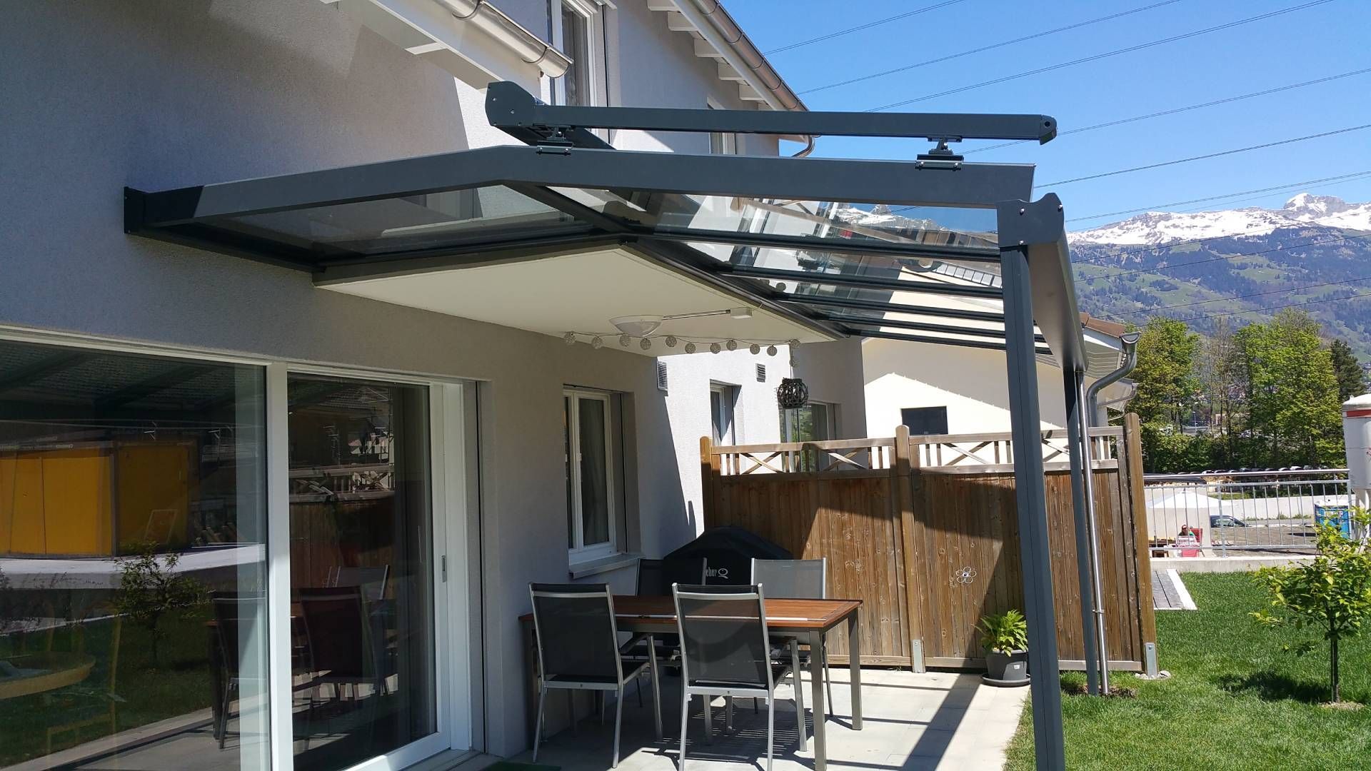 Terrasse mit schwarzer Pergola und Gartentisch neben einem Haus mit Blick auf die Berge