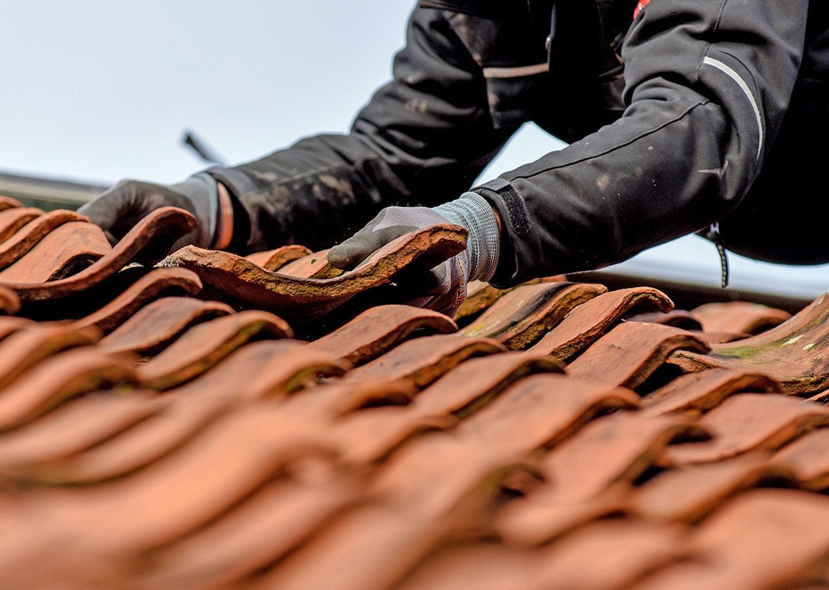 Gros plan d'un homme avec des gants qui change une tuile  cassé