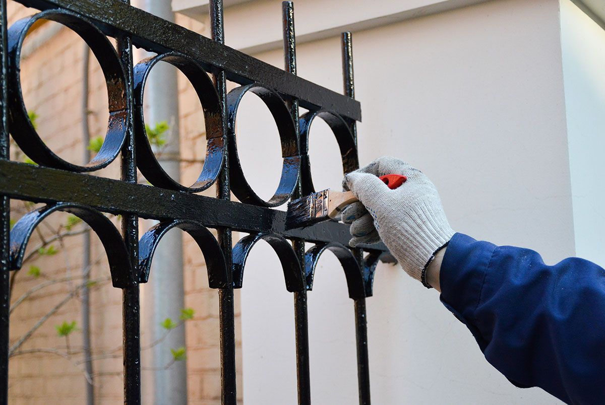 Homme qui peint une clôture en ferraille en noir
