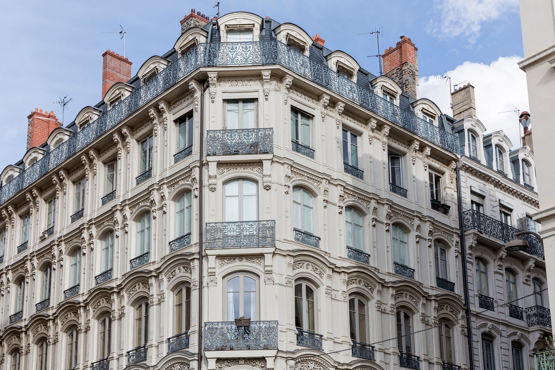 Immeuble beige orné, avec façade détaillée, vue d'angle, balcons et lucarnes.