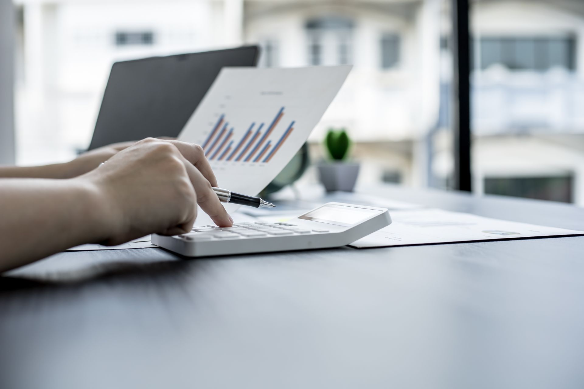 Des mains utilisent une calculatrice sur un bureau avec un ordinateur portable et un graphique à barres.