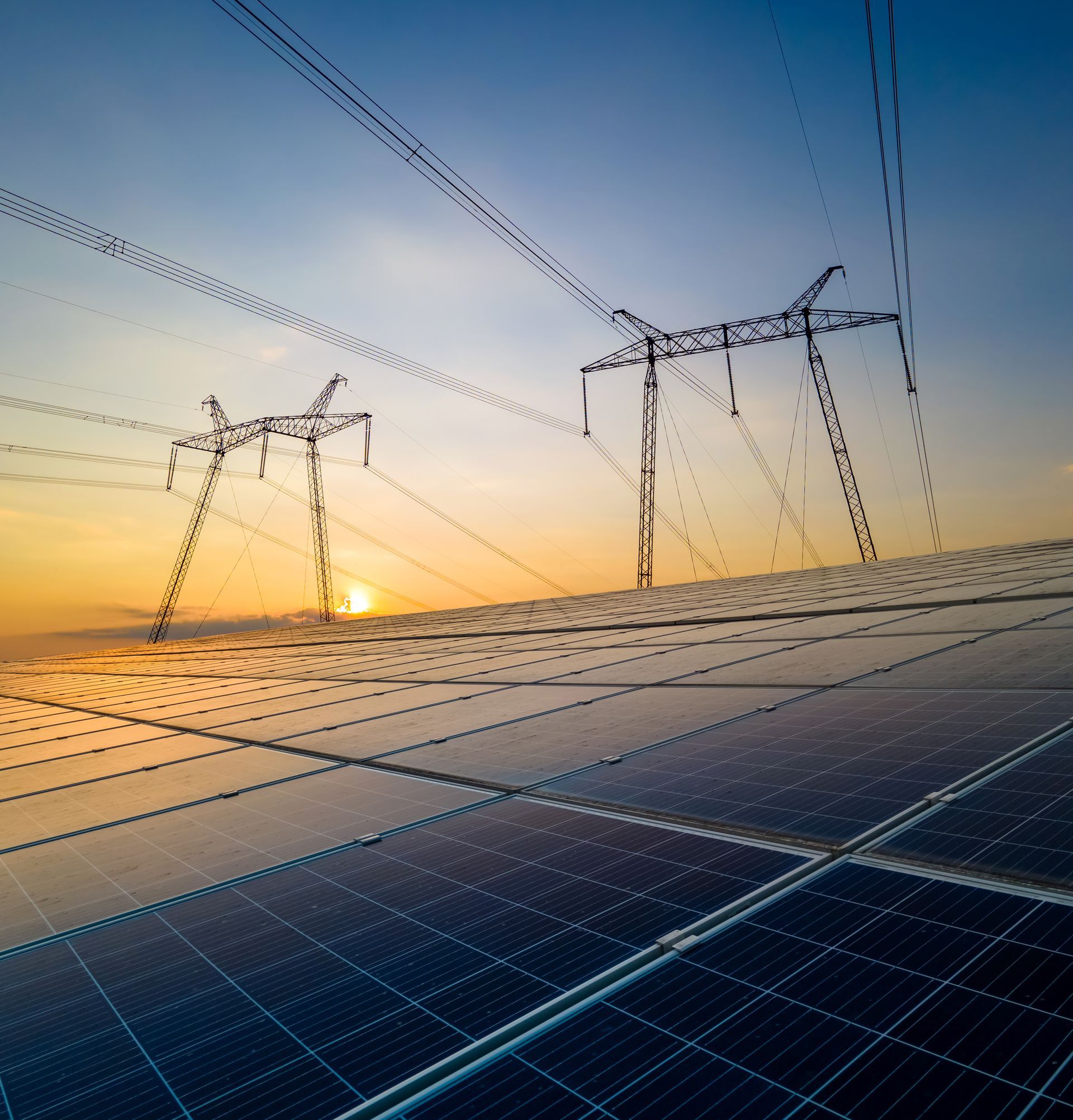 Panneaux solaires, lignes électriques et pylônes au coucher du soleil.