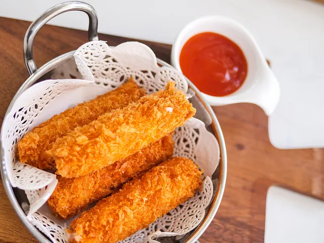Un tazón de palitos de mozzarella fritos junto a un tazón de kétchup.
