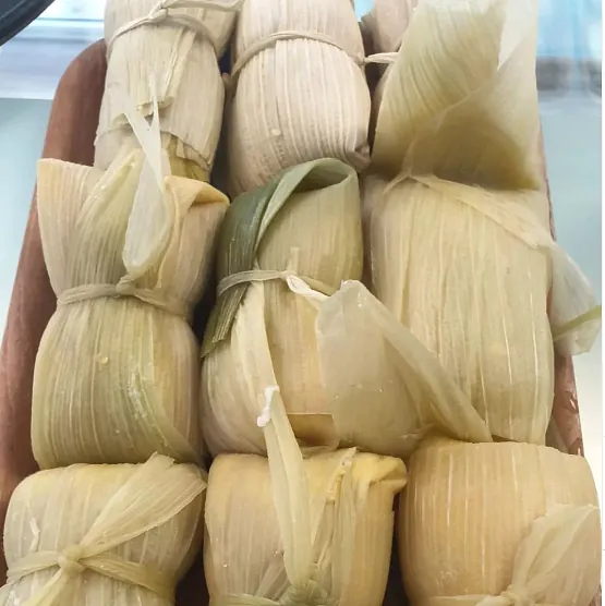 Un montón de tamales envueltos en hojas de maíz se apilan uno encima del otro.