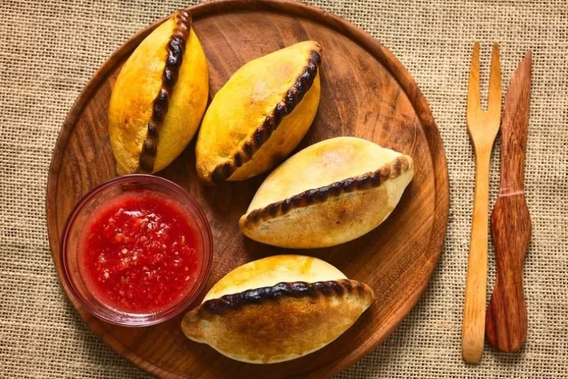 Un plato de madera cubierto con cuatro pasteles y un tazón de salsa.