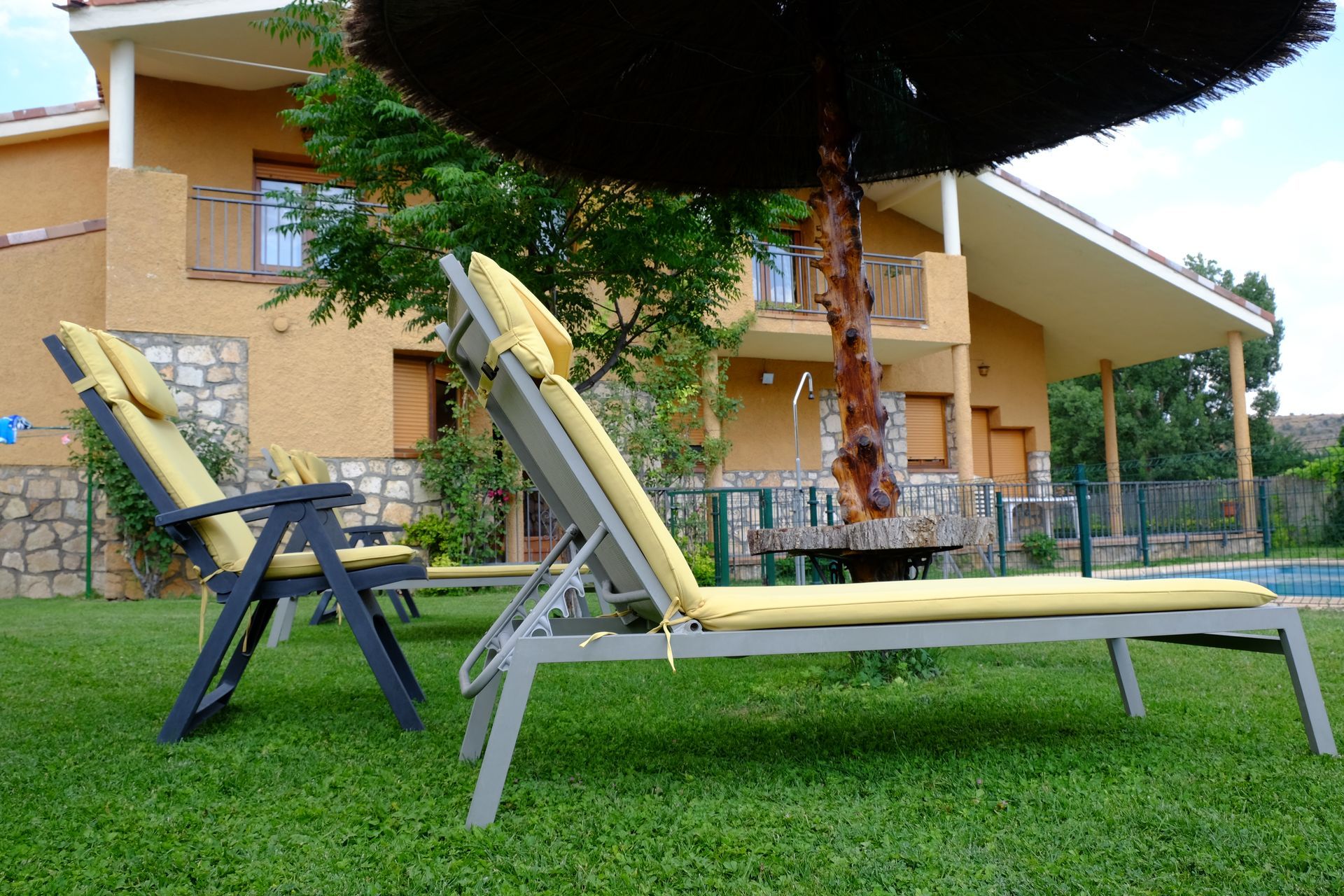 Tumbonas en un césped verde con una casa al fondo y una gran sombrilla encima.