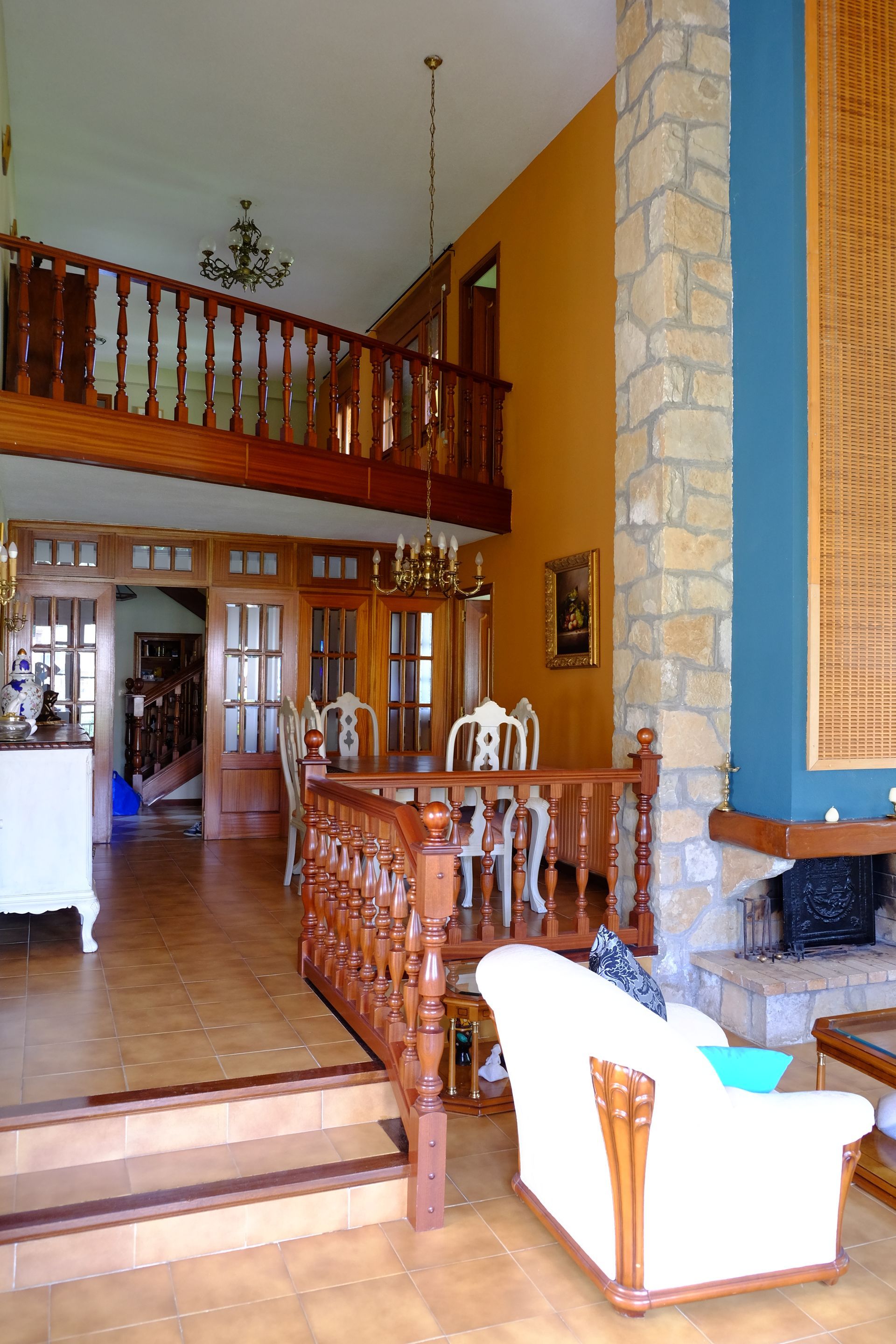 Vista interior de una casa con escalera, comedor, sala con chimenea y balcón.