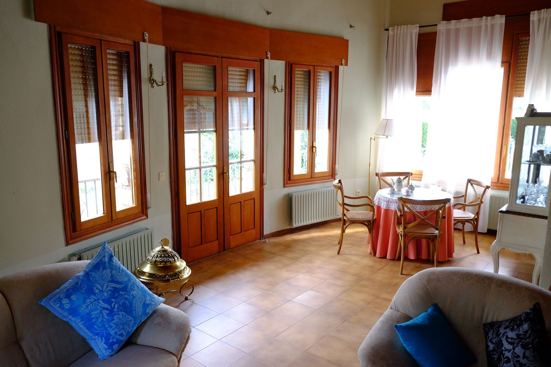 Sala de estar con ventanas y puertas de madera, mesa de comedor y dos sillones.