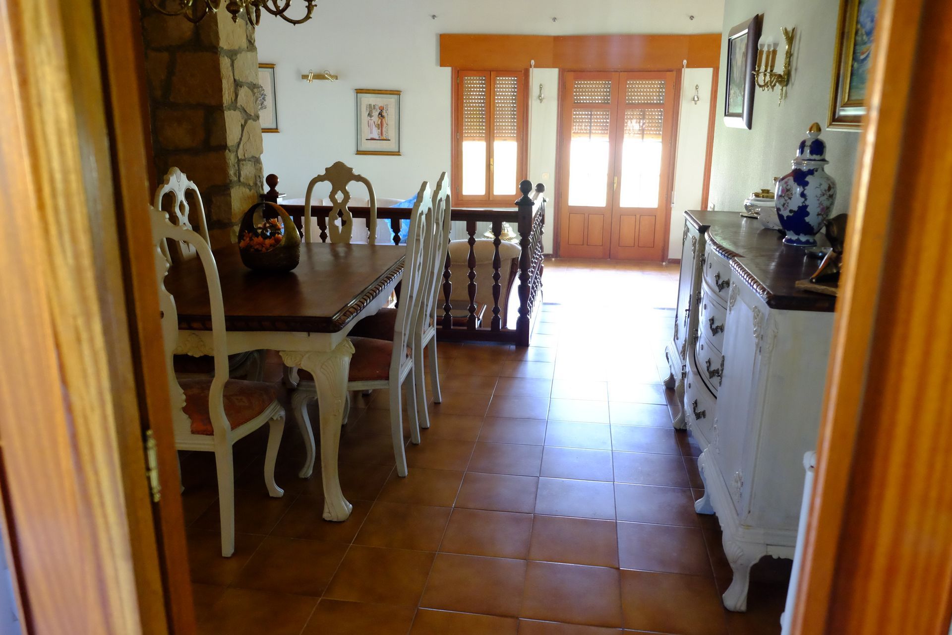 Comedor con mesa y sillas de madera, buffet y puerta de entrada abierta.