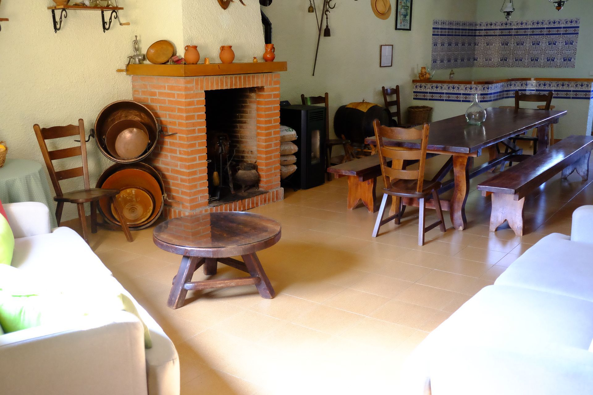Comedor rústico con chimenea de ladrillo, mesa larga de madera y decoración con utensilios de cocina variados.