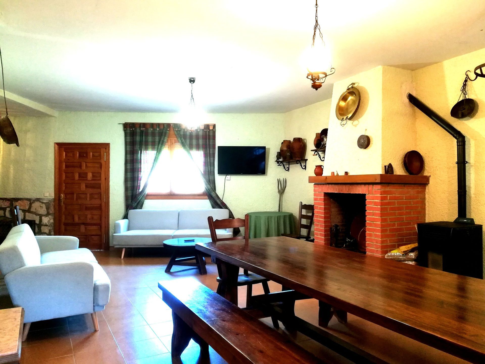 Salón con chimenea, mesa larga de madera, dos sofás, TV y elementos decorativos.
