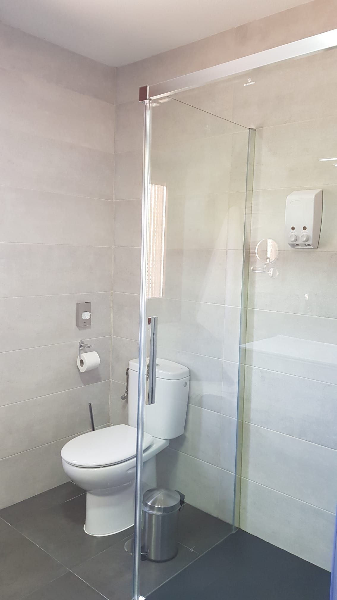 Baño con inodoro, paredes grises y puerta de ducha de cristal.