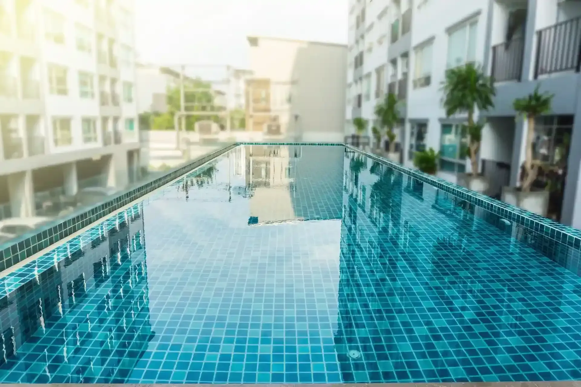 Piscina en la azotea con azulejos turquesas que reflejan el cielo, rodeada de edificios.